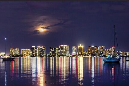 Sarasota Skyline at Night Reflecting on the Water with moon in the sky.